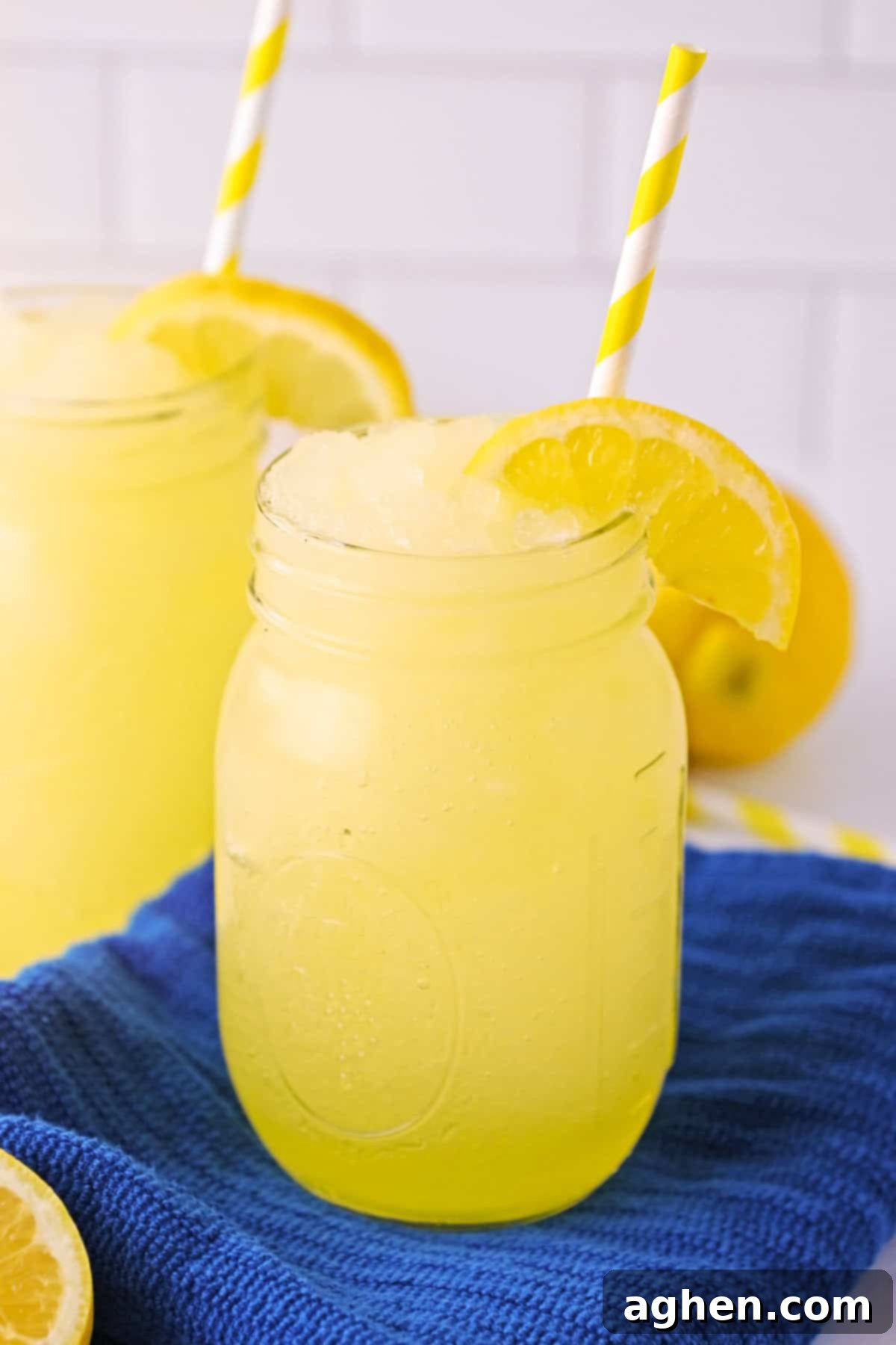 Frozen Lemonade Bliss 2 Frozen lemonade slushies garnished with slice of lemon and served in mason jars with straws.