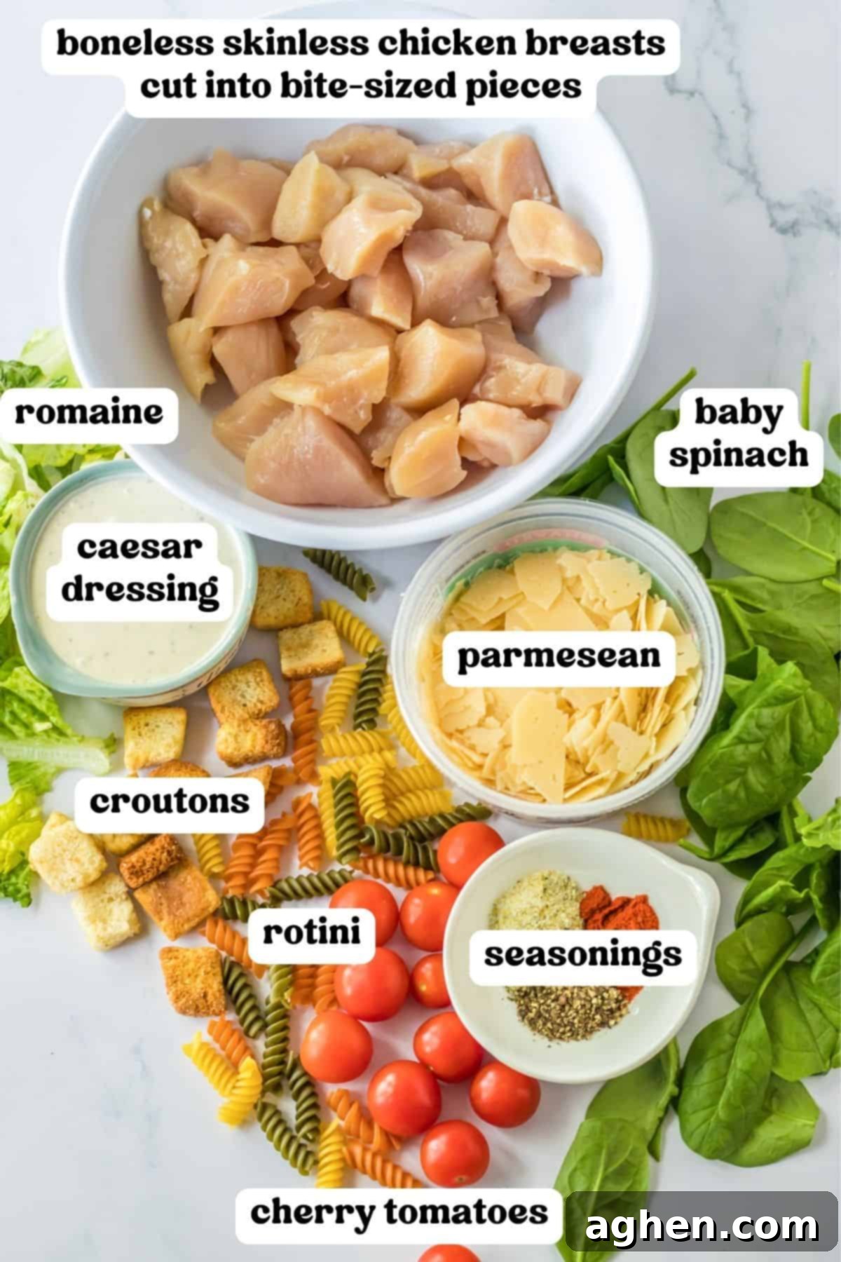 An organized display of fresh ingredients for Caesar Chicken Pasta Salad: seasoned bite-sized chicken breasts, crisp romaine lettuce, fresh baby spinach, halved cherry tomatoes, shaved Parmesan cheese, tri-colored rotini pasta, and golden croutons.