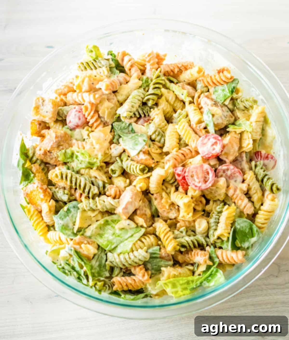 The fully dressed Caesar chicken pasta salad in a large serving bowl, ready to be chilled.