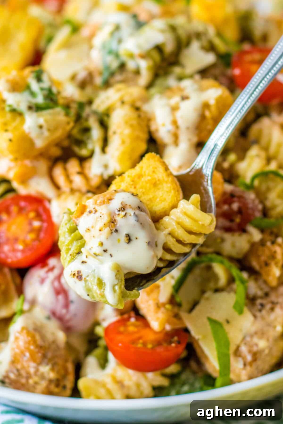 A forkful of creamy Chicken Caesar Pasta Salad, showcasing the chicken, pasta, lettuce, and tomatoes.