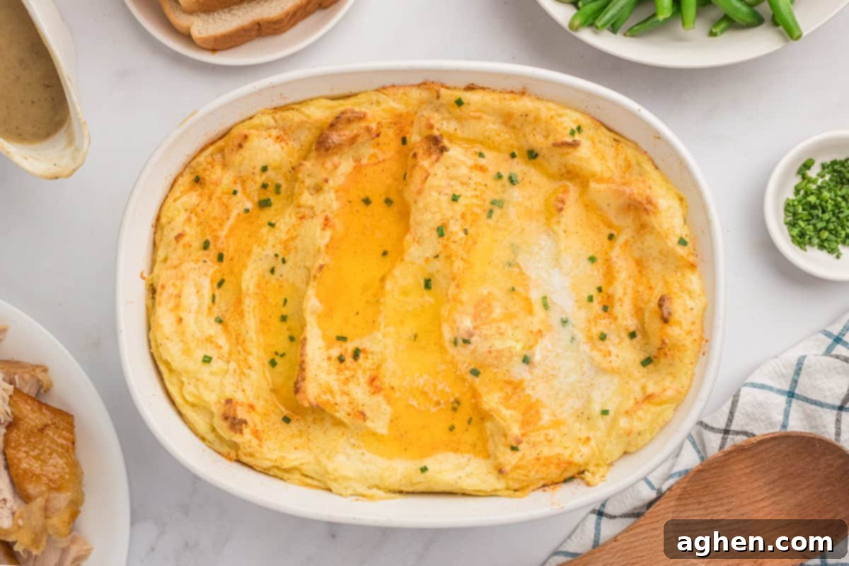 A large baking dish of Party Mashed Potatoes with Cream Cheese sits prominently on a festively adorned holiday dinner table, surrounded by other delicious dishes, ready for serving.