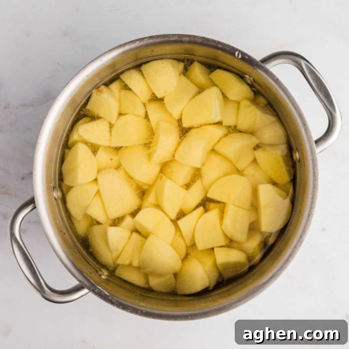 Peeled and uniformly cubed potatoes are submerged in a large pot of cold water, ready for boiling.