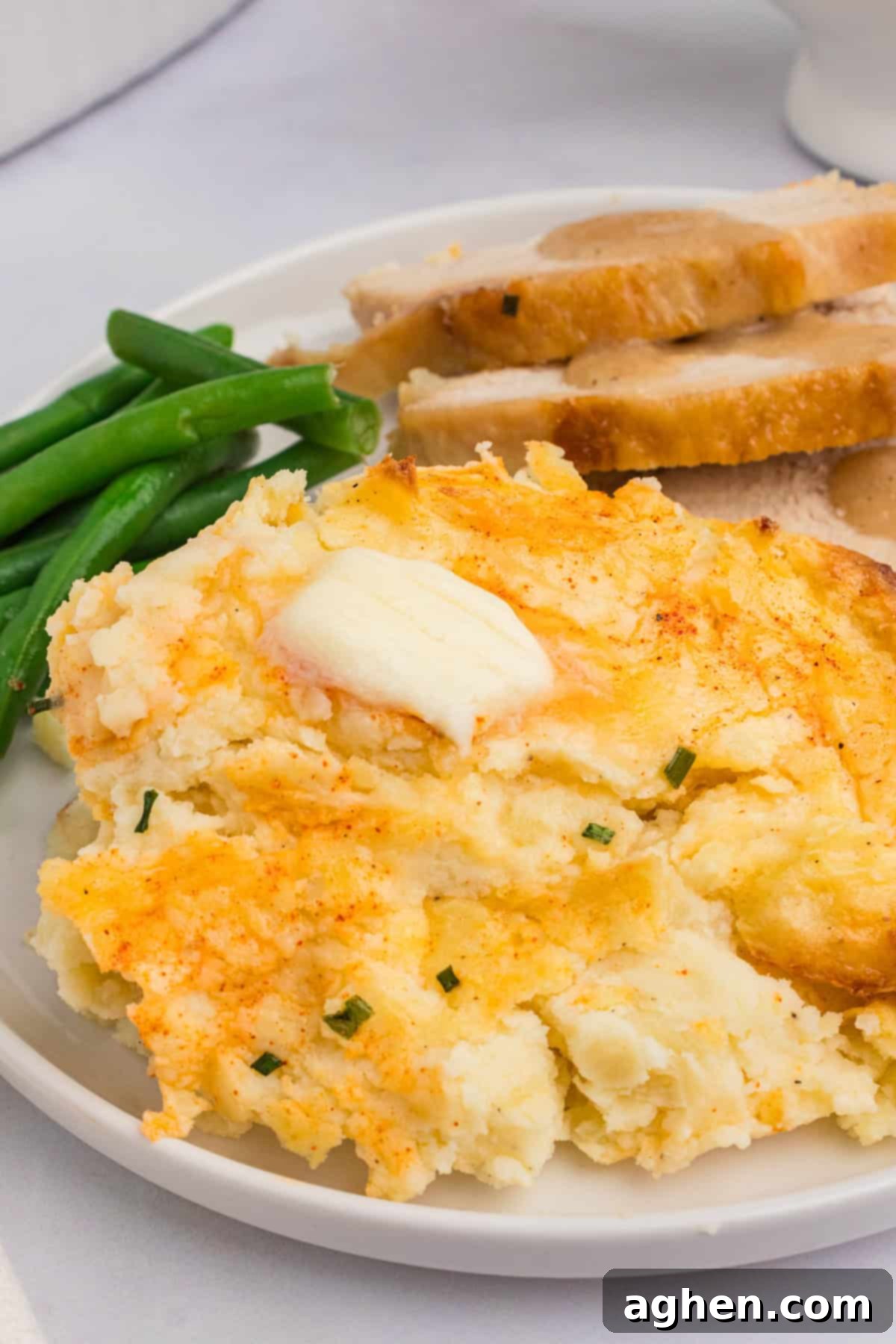 A perfectly portioned serving of party mashed potatoes on a white plate, accompanied by vibrant green beans and slices of succulent roasted turkey, creating a complete and inviting meal.