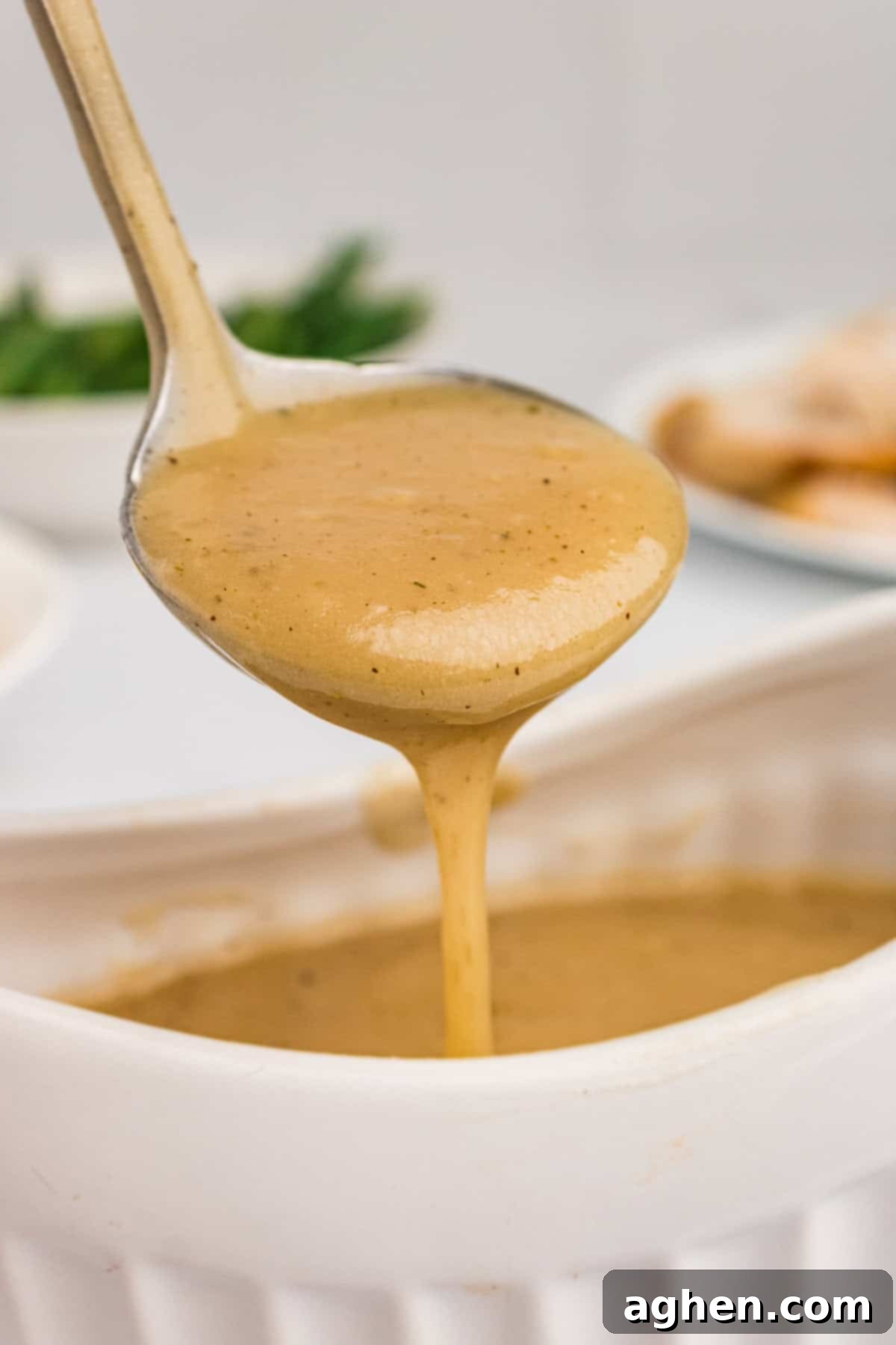 Turkey gravy without drippings in a gravy ladle, gracefully dripping into a white gravy boat below it, highlighting the rich, smooth texture.