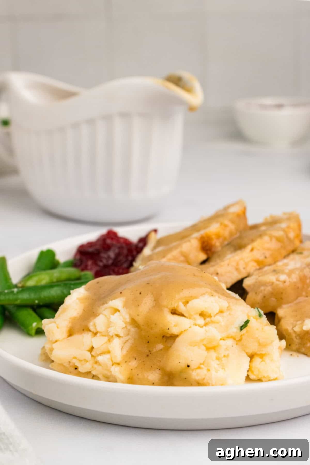 A festive Thanksgiving dinner spread featuring creamy mashed potatoes with gravy, sliced roast turkey, a bowl of cranberry sauce, and a full gravy boat in the background.