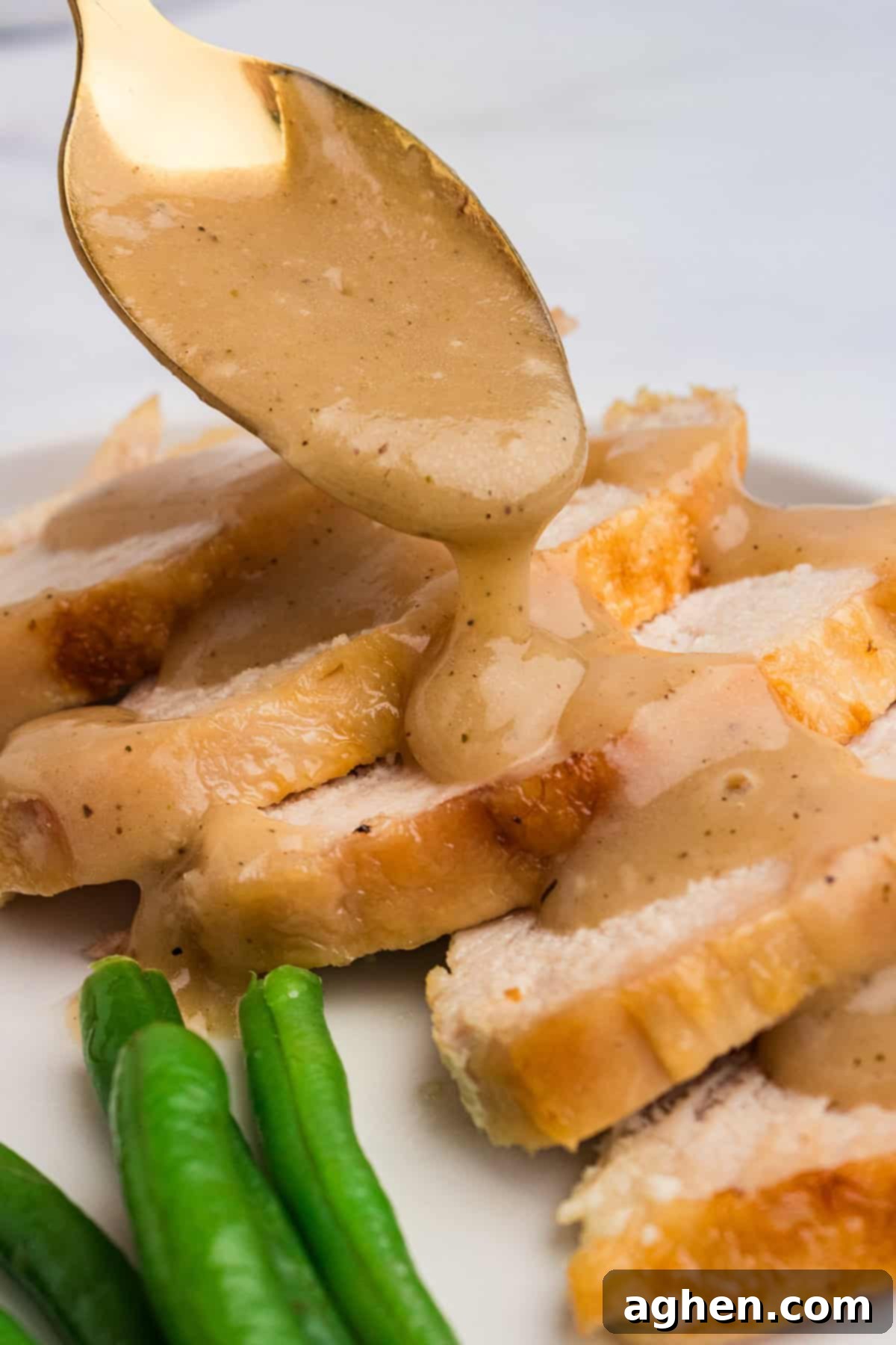 Thanksgiving gravy generously drizzled over tender slices of roasted turkey on a white platter, creating a mouth-watering visual.