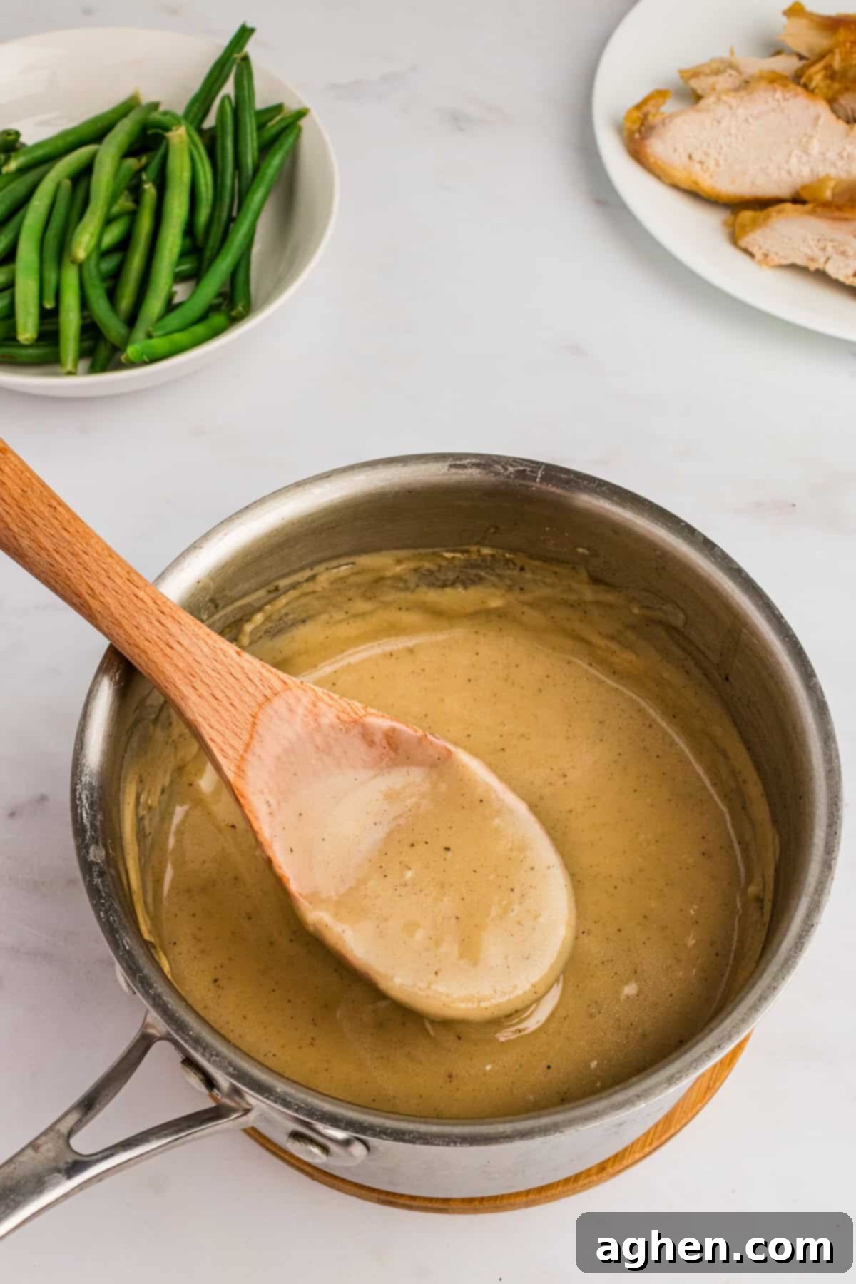 A pot of thick, homemade gravy sits beside a beautifully roasted turkey and vibrant green beans, showcasing a complete and appealing meal.