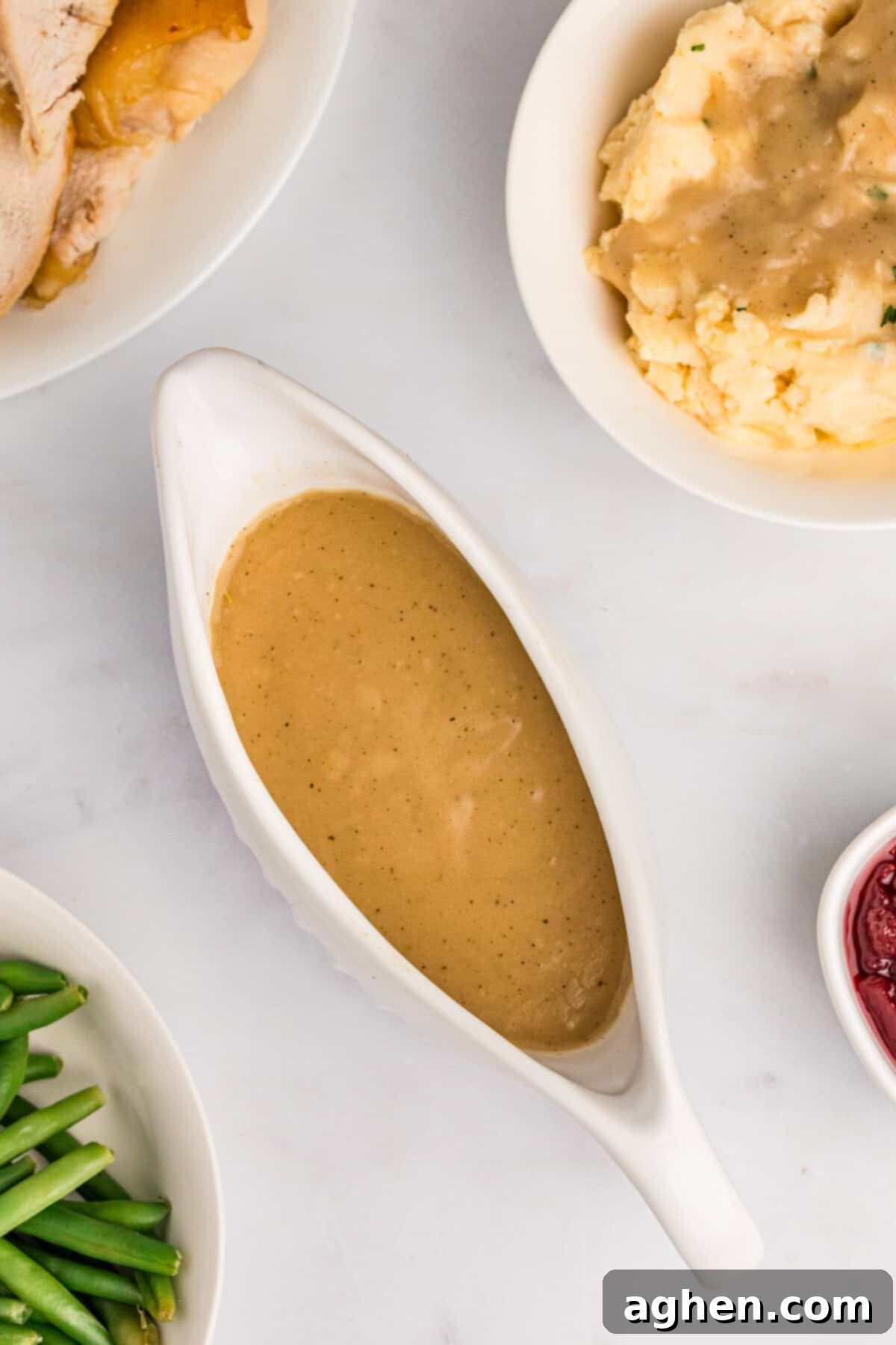 Easy turkey gravy without drippings, elegantly presented in a gravy boat, surrounded by tender green beans, succulent turkey, and creamy mashed potatoes.
