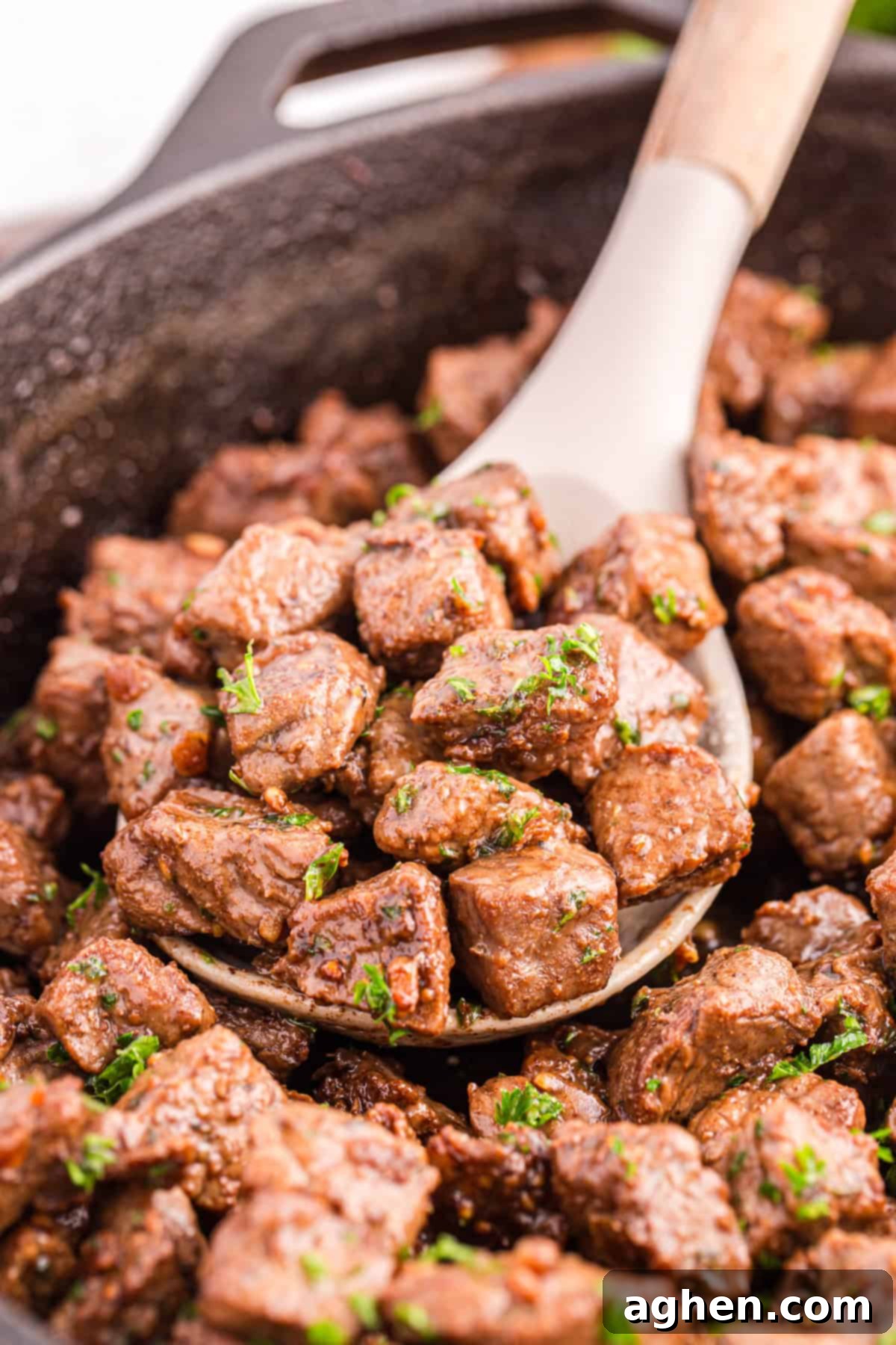 Spoon lifting tender garlic butter steak bites out of a skillet, coated in butter sauce.