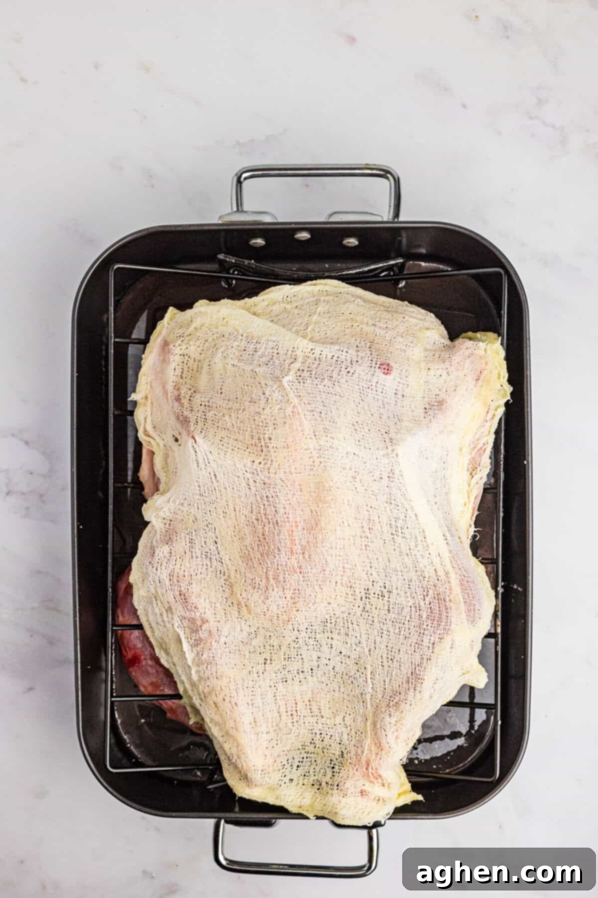 Butter soaked cheesecloth draped over a turkey in roasting pan.