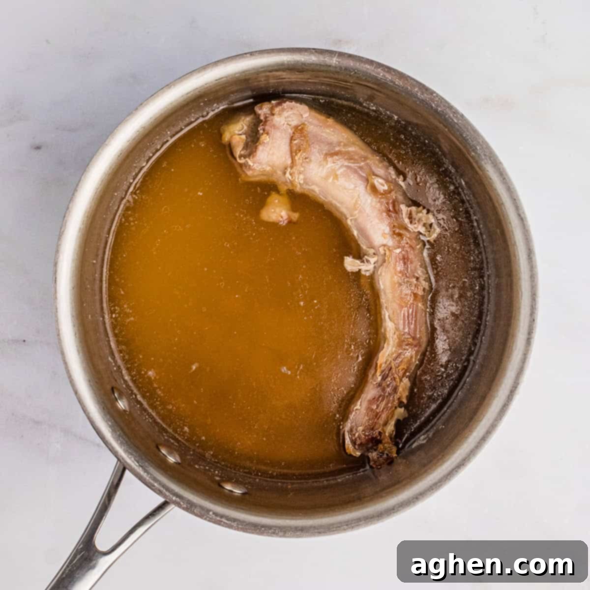 Turkey neck simmering in broth and water in a saucepan.