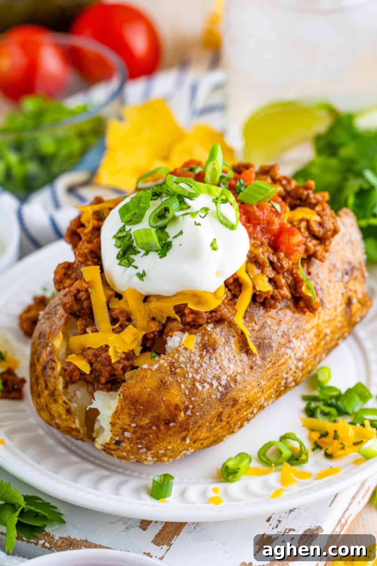 A baked potato split open and generously filled with taco-seasoned ground beef, topped with shredded cheese, a dollop of sour cream, fresh salsa, cilantro, and sliced green onions.