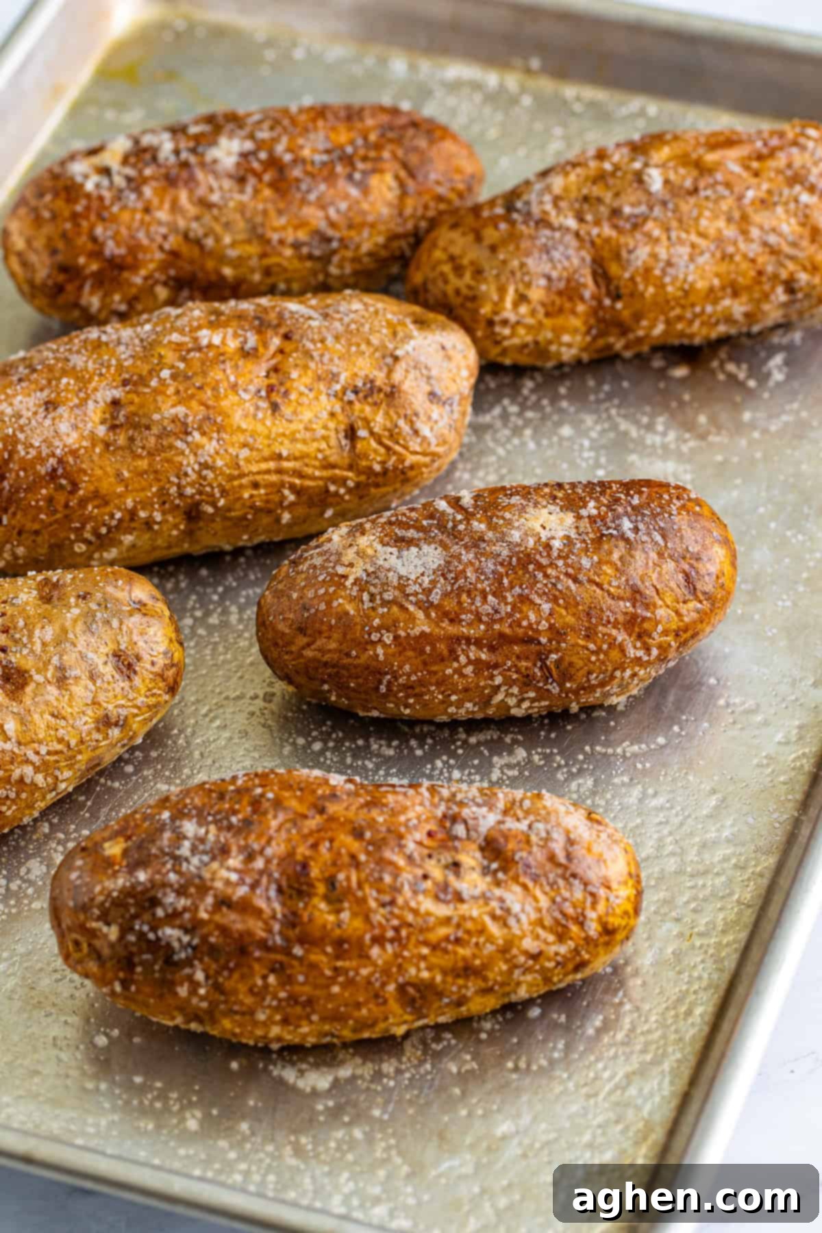 Freshly baked potatoes with crisp, salty skin resting on a sheet pan, ready to be filled.