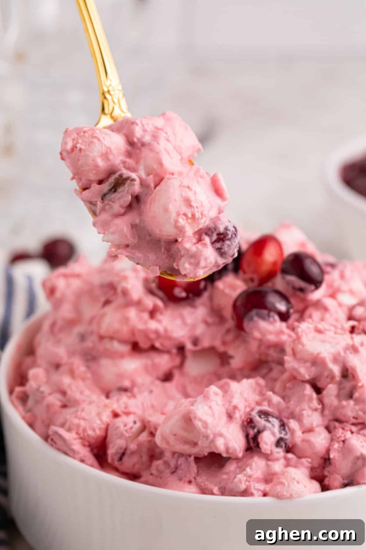 Spoonful of cranberry fluff salad with marshmallows and pecans over a bowl of the pink fluff.