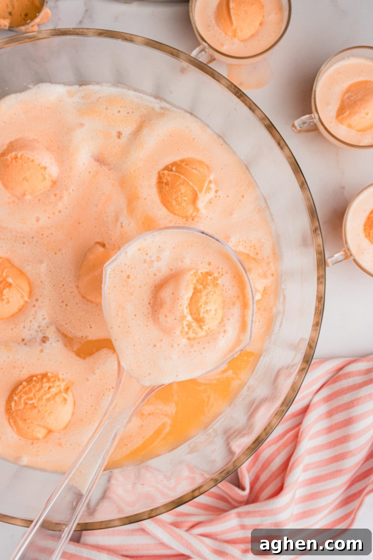 Champagne Punch with Sherbet in large glass punch bowl with glasses of punch next to it.