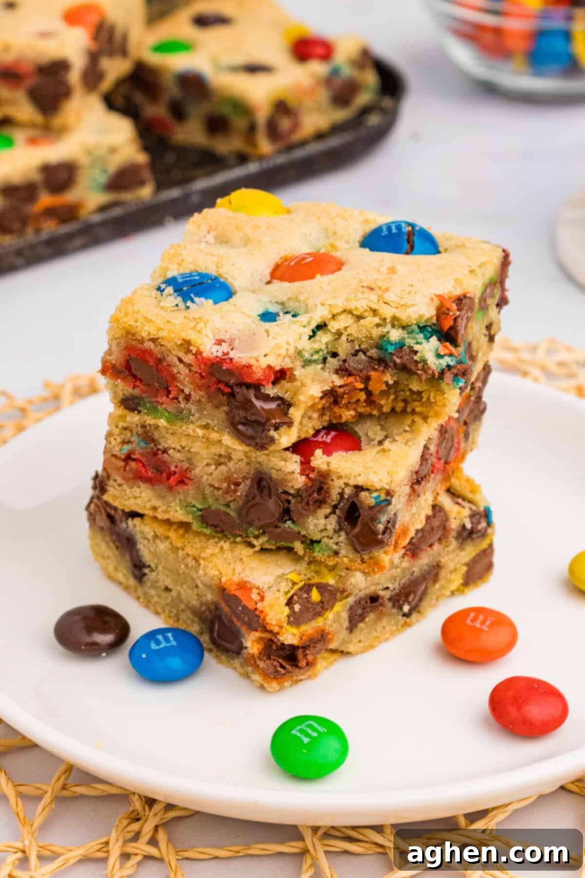 Three thick M&M cookie bars stacked on top of each other, with the top bar missing a bite, highlighting the soft interior.