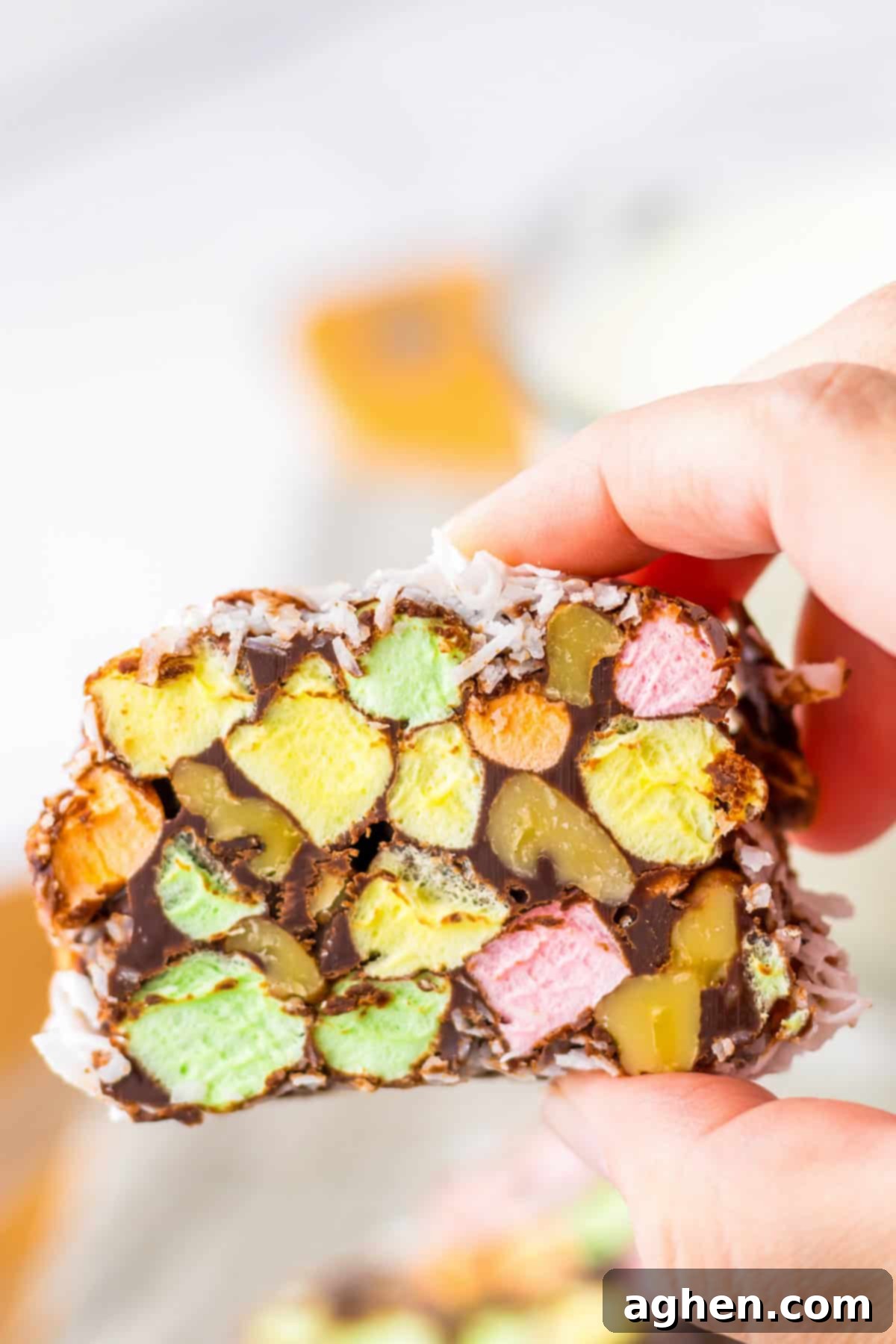 Holding a no-bake church window cookie with bright marshmallow and nut centers, chocolate coating, and a coconut finish.