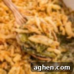 Spoonful of green bean casserole with Worcestershire sauce and crispy fried onions being served with a wooden spoon.