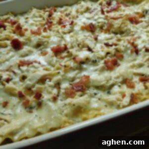 Close-up of the fully cooked Chicken and Bacon Alfredo Lasagna in a casserole dish, topped with melted cheese and fresh herbs.