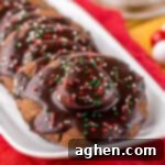 Hot chocolate cookies topped with marshmallows, chocolate icing, and festive sprinkles on a white platter.