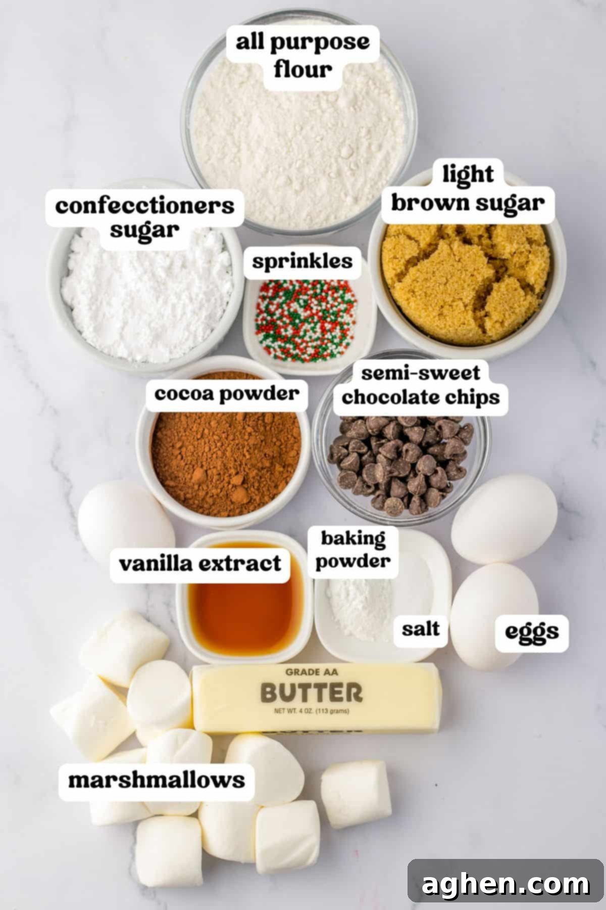 Ingredients for hot chocolate cookies, including flour, brown sugar, cocoa powder, marshmallows, chocolate chips, and festive sprinkles.