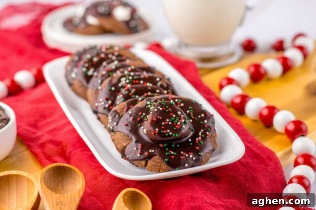 Hot chocolate cookies with marshmallows, chocolate icing, and Christmas sprinkles on a white platter.