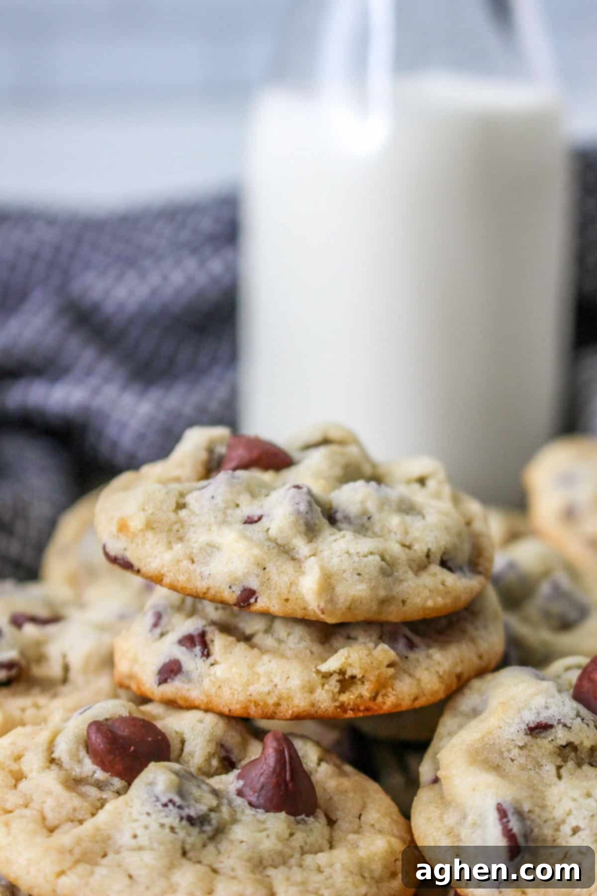 A close-up of soft and chewy yogurt chocolate chip cookies stacked on a plate, served with a glass of milk in the background.