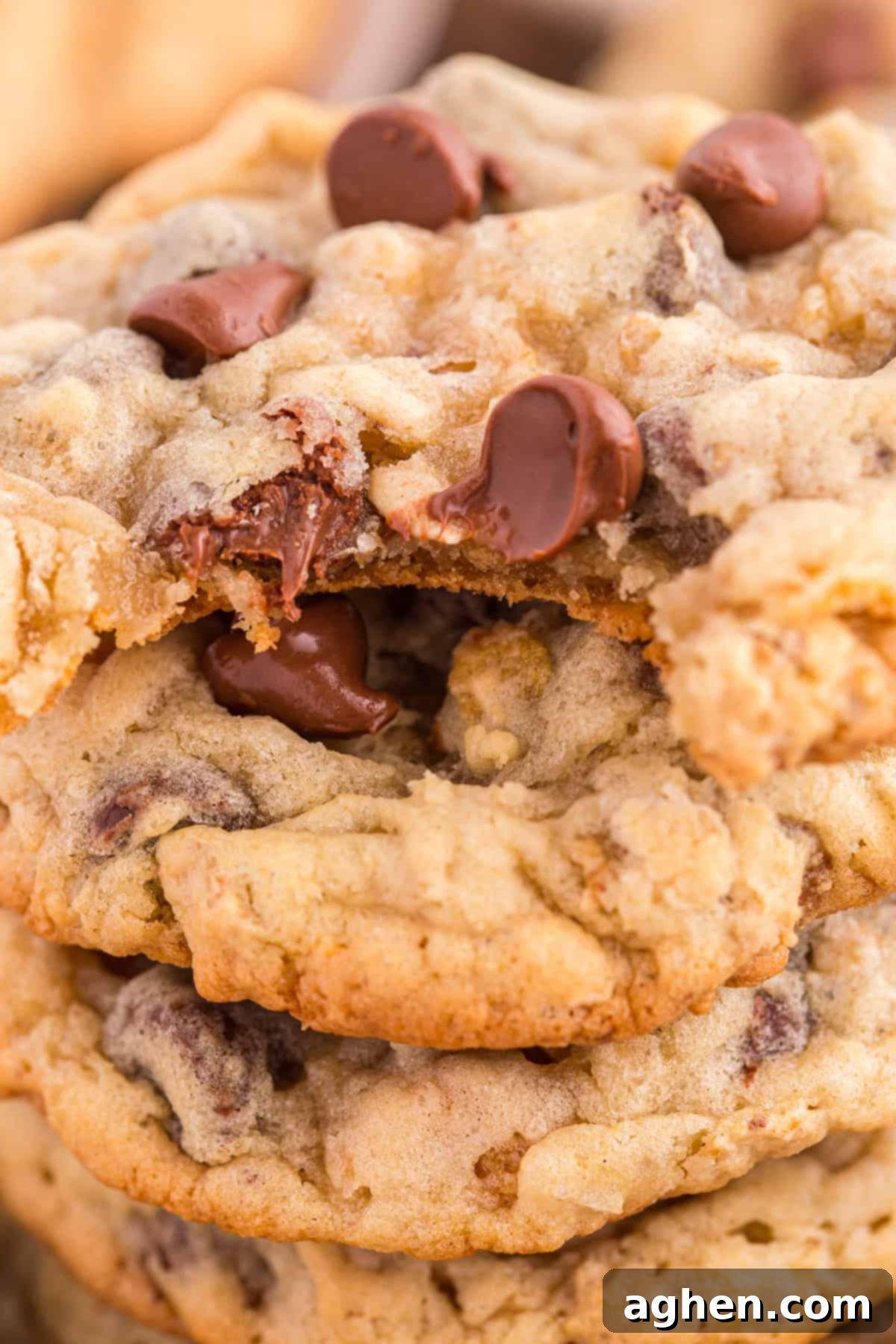 A stack of freshly baked Ranger Cookies with visible chocolate chips and oats. One cookie has a bite taken out of it, revealing its gooey chocolate center and crispy, textured exterior, inviting a taste.