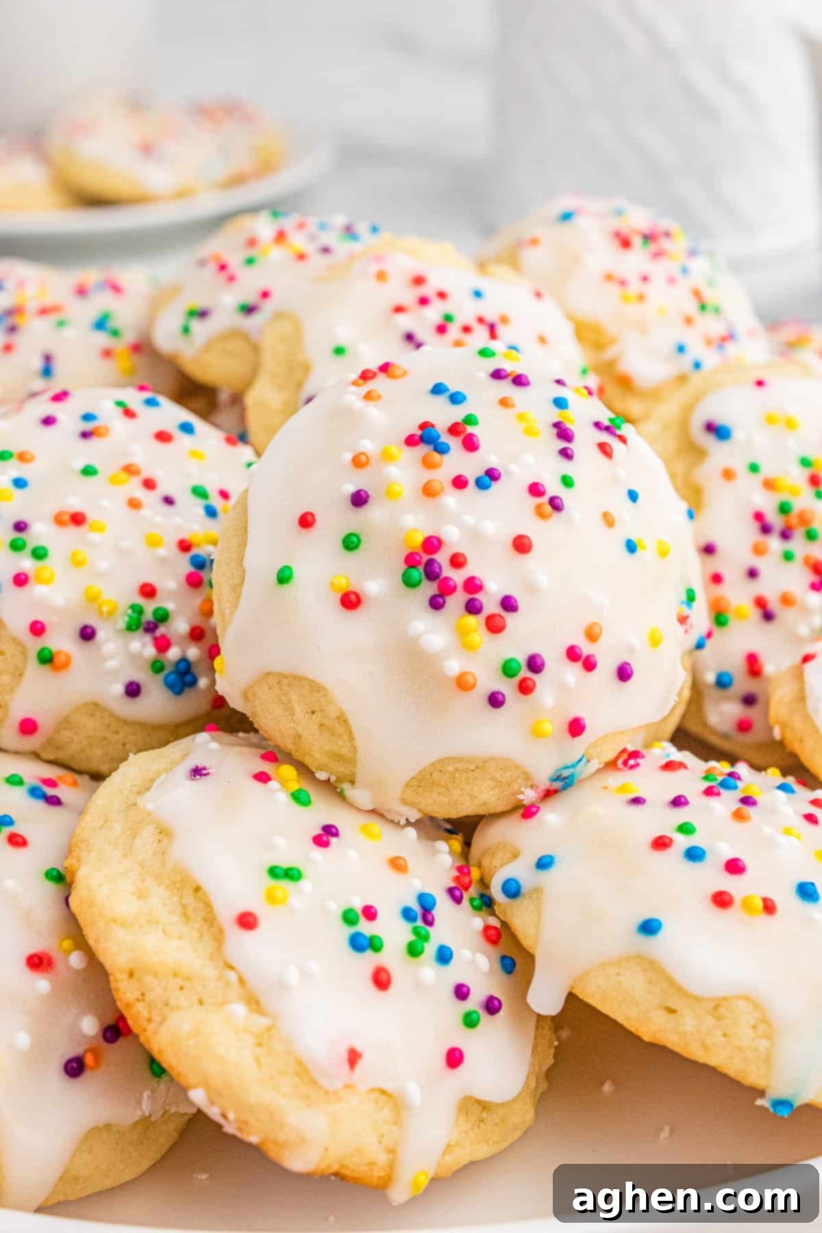 A close-up of Italian ricotta cookies topped with glossy white icing and colorful sprinkles, stacked on a plate. The soft texture of the cookies and the vibrant sprinkles create a festive and inviting presentation.