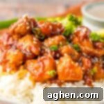 Bourbon chicken like at the mall food court with sesame seeds and green onions over rice, with broccoli in the background.