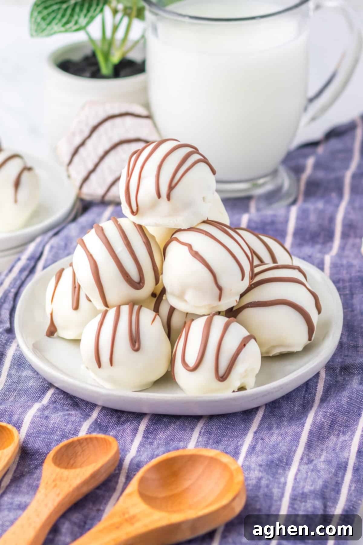 A close-up of a white plate stacked with Little Debbie Zebra Cake Balls- round truffles coated in white chocolate and decorated with thin milk chocolate drizzles.