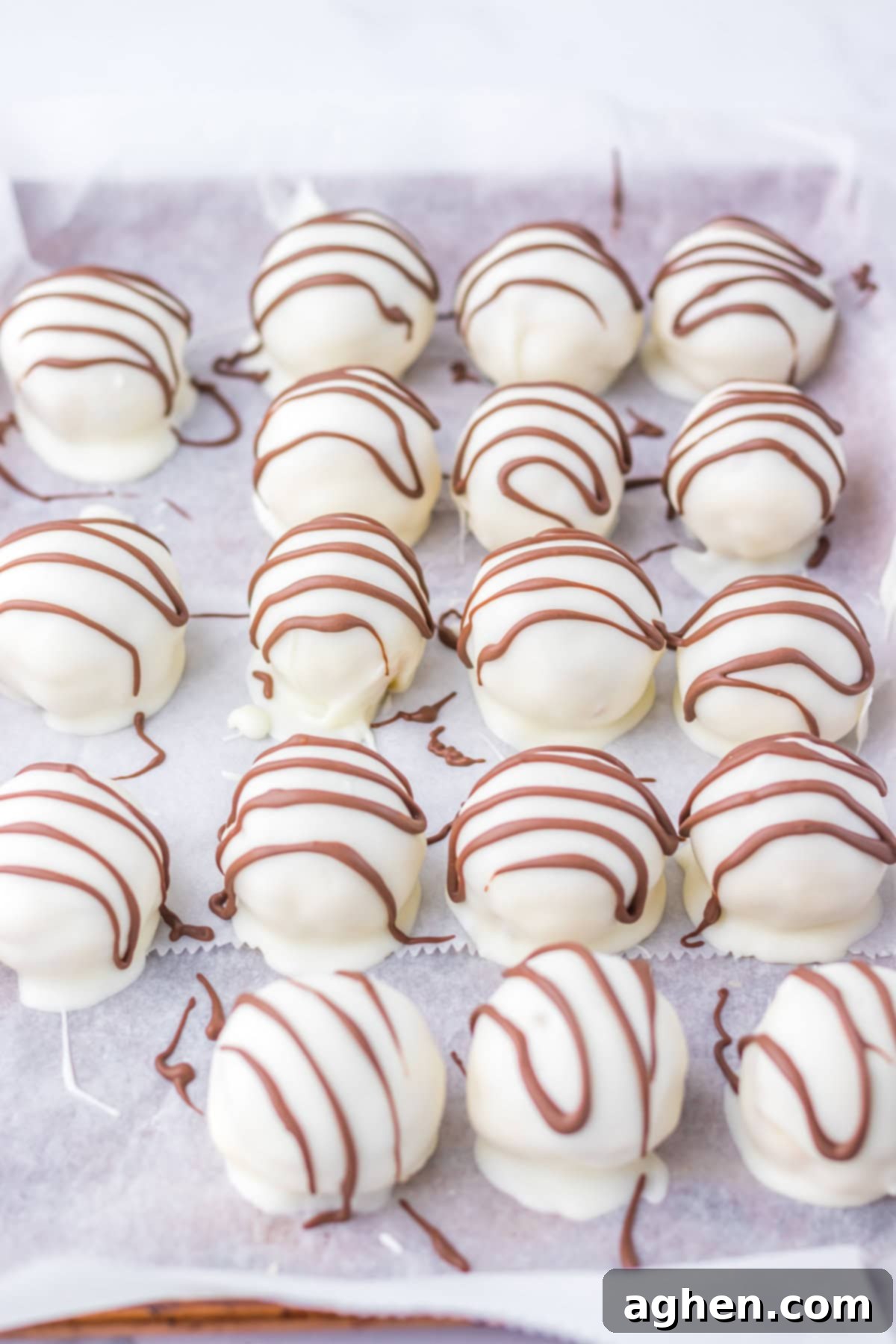 Rows of white chocolate-coated Little Debbie zebra cake truffles drizzled with milk chocolate on parchment paper.