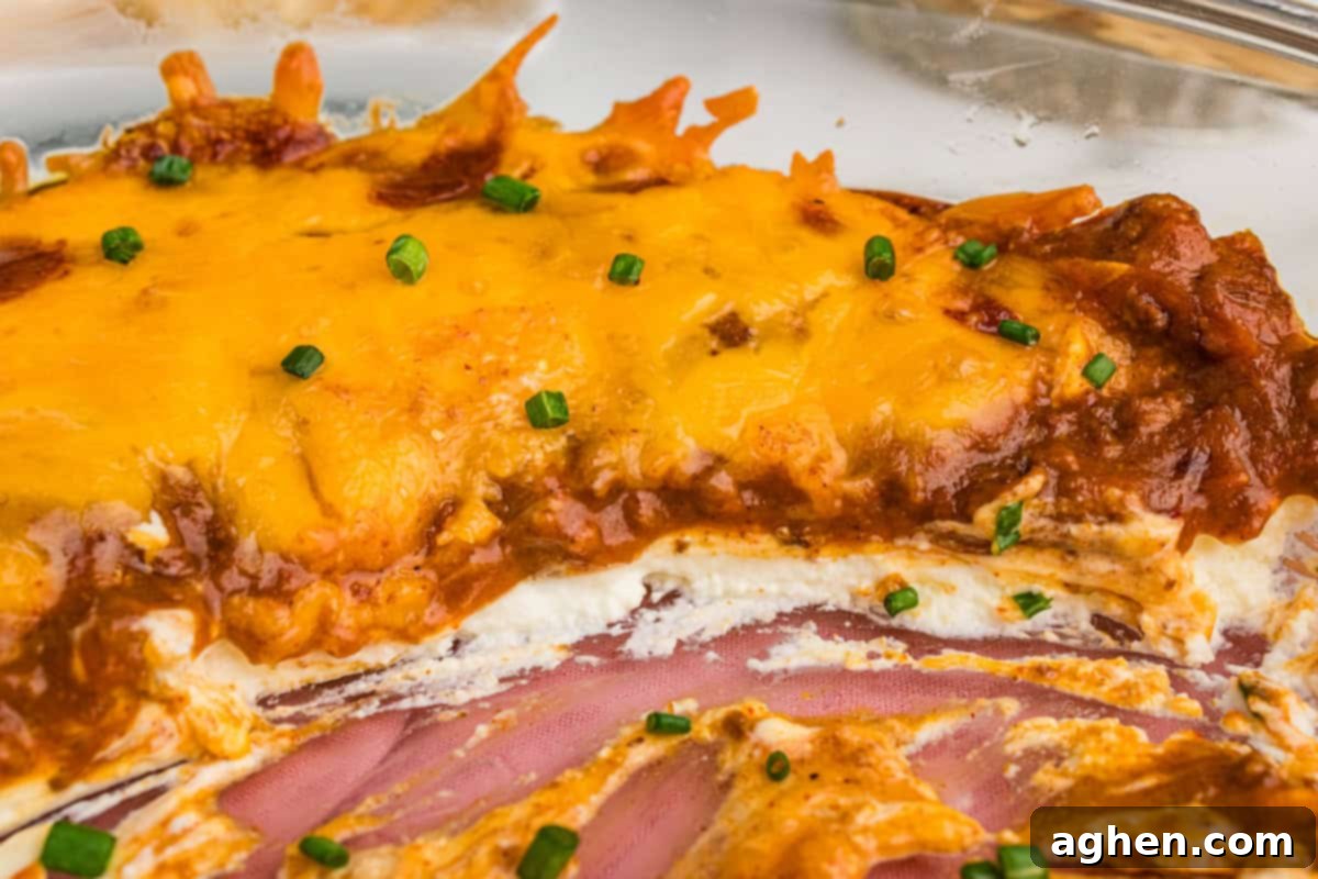 A close-up of the baked Hormel chili cheese dip with a section scooped out, revealing layers of cream cheese, chili, and cheddar topped with chives.