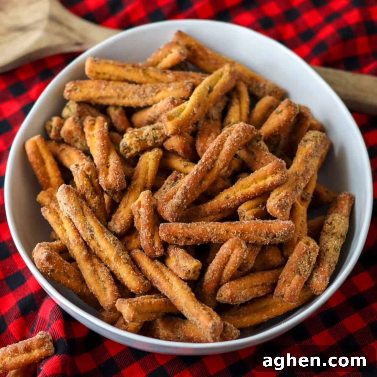 Spiced Pretzel Rods 2 A bowl of seasoned pretzel sticks, similar to Dot's pretzels, on a red plaid background, showcasing their golden-brown color and generous seasoning.