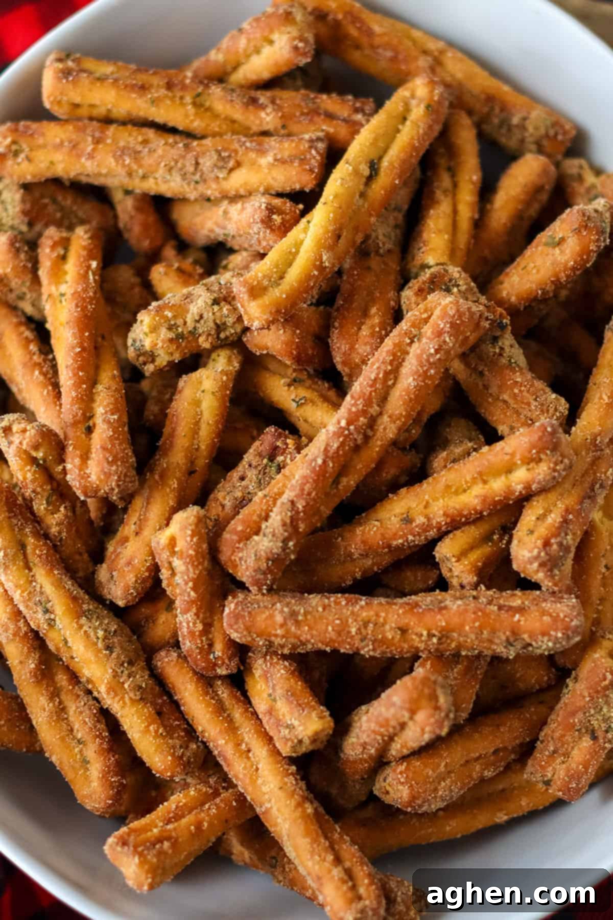 Spiced Pretzel Rods 6 A tightly cropped view of golden-brown pretzel sticks in a pristine white bowl, highlighting their coarse texture and rich, even seasoning. The pretzels are generously coated with a blend of savory spices, reminiscent of popular flavored pretzel brands.