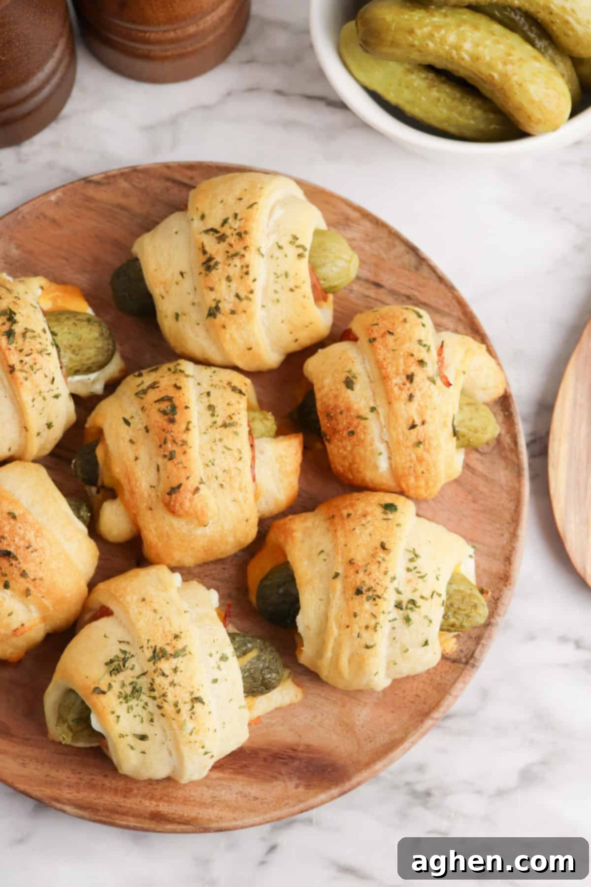 A plate with golden brown baked pickles in a blanket topped with herbs.