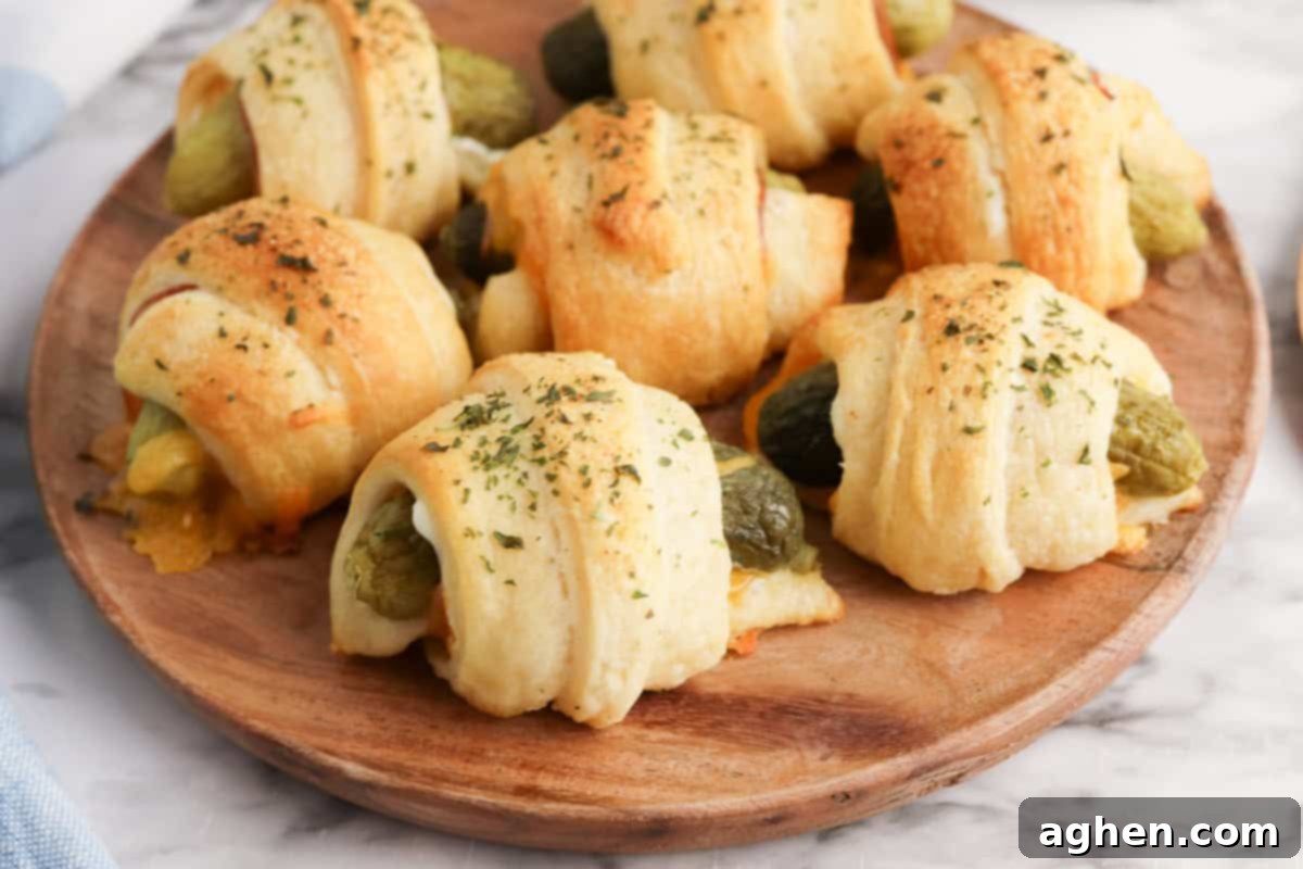 A close-up view of crescent roll-wrapped pickles on a round wooden plate. The rolls are golden and sprinkled with dried herbs