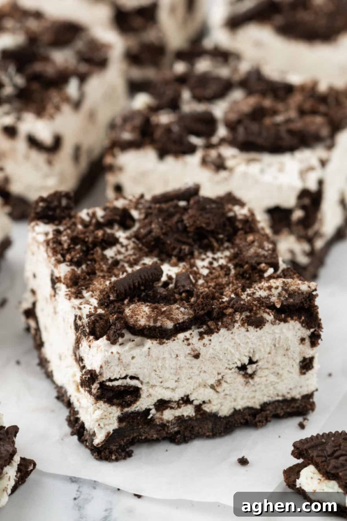 Oreo cheesecake bars on parchment paper. Each bar features distinct layers of a chocolate cookie crust, creamy cheesecake filling, and crushed Oreo topping.