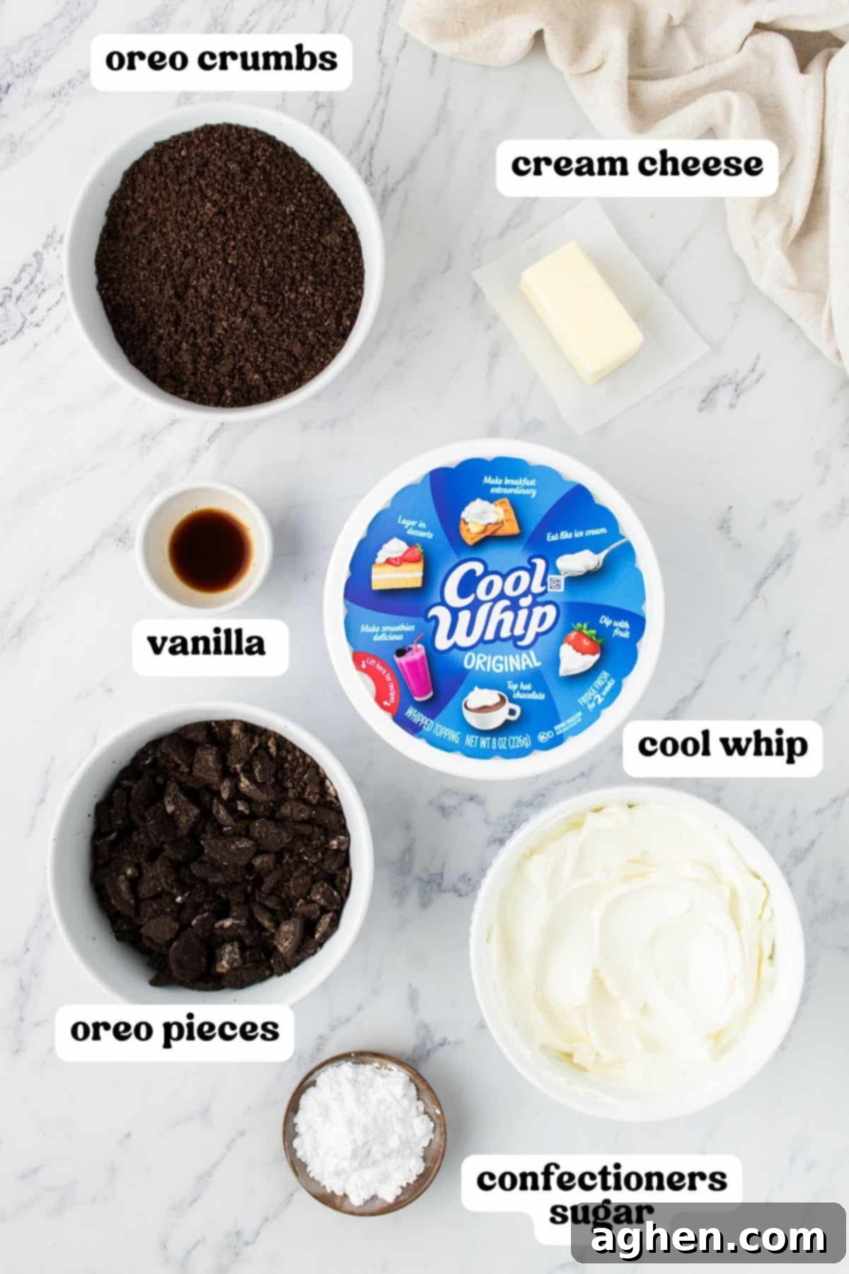 Ingredients for no-bake Oreo cheesecake bars, including Oreo crumbs, cream cheese, vanilla, Cool Whip, Oreo pieces, and confectioners sugar.