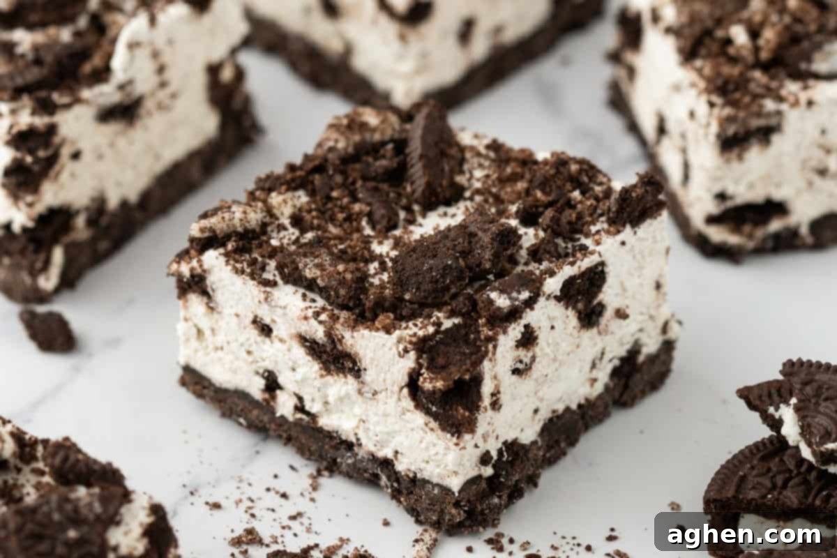 A close-up of a single no-bake Oreo cheesecake bar with additional bars and oreo cookie crumbs scattered around.