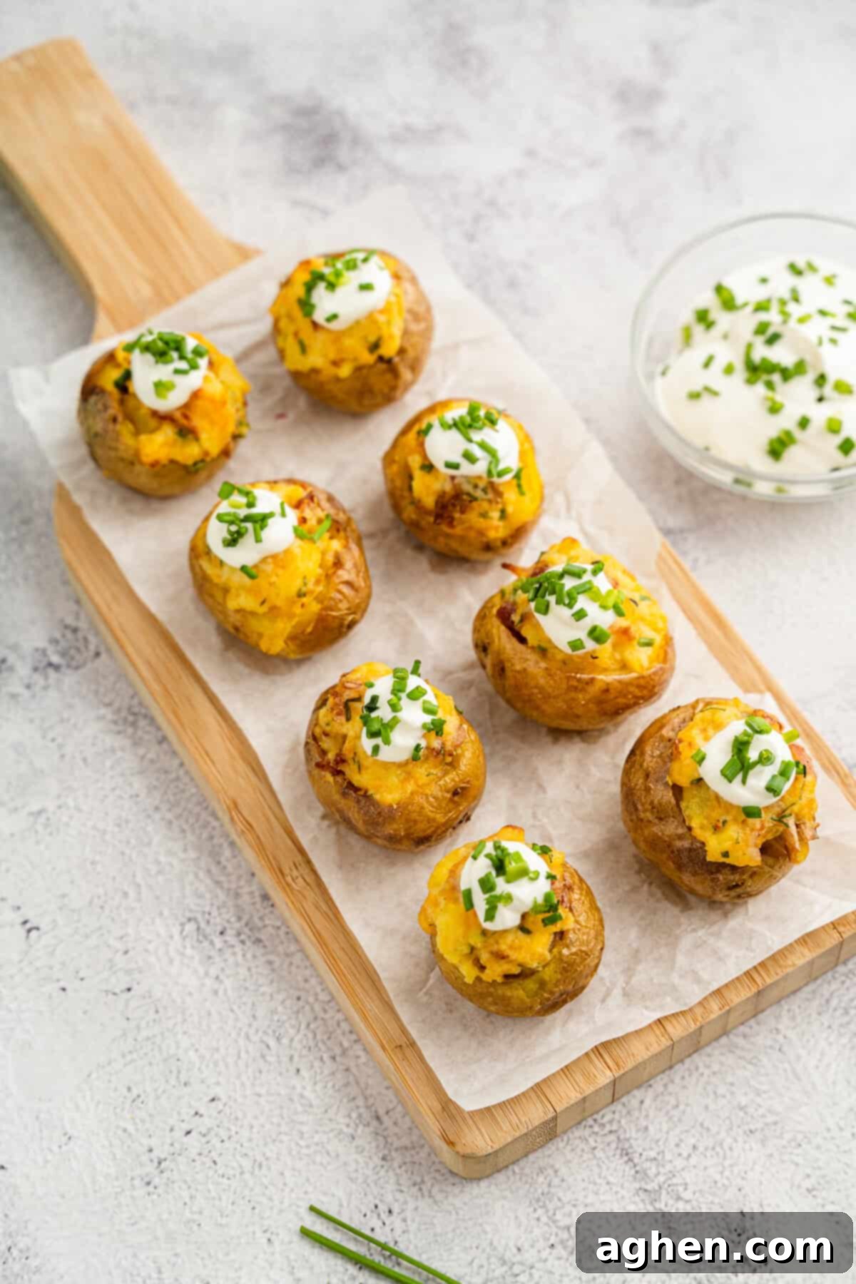 Bite-sized mini loaded potatoes arranged on a wooden serving board and topped with sour cream and chives, ready to be served as a delicious appetizer.