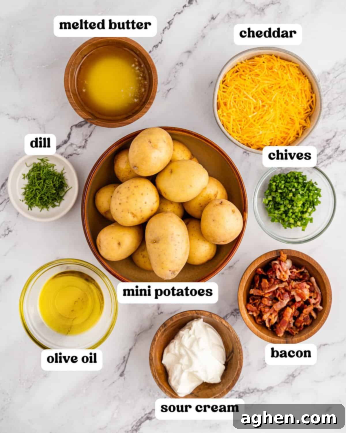 Overhead view of all the fresh ingredients for loaded mini baked potatoes neatly arranged on a white marble surface, including mini golden potatoes, shredded cheddar cheese, crispy bacon, fresh sour cream, vibrant chives, aromatic dill, olive oil, and melted butter, with each ingredient clearly labeled.