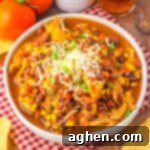 A bowl of chicken taco soup recipe topped with shredded cheese and green onions, surrounded by tortilla chips.