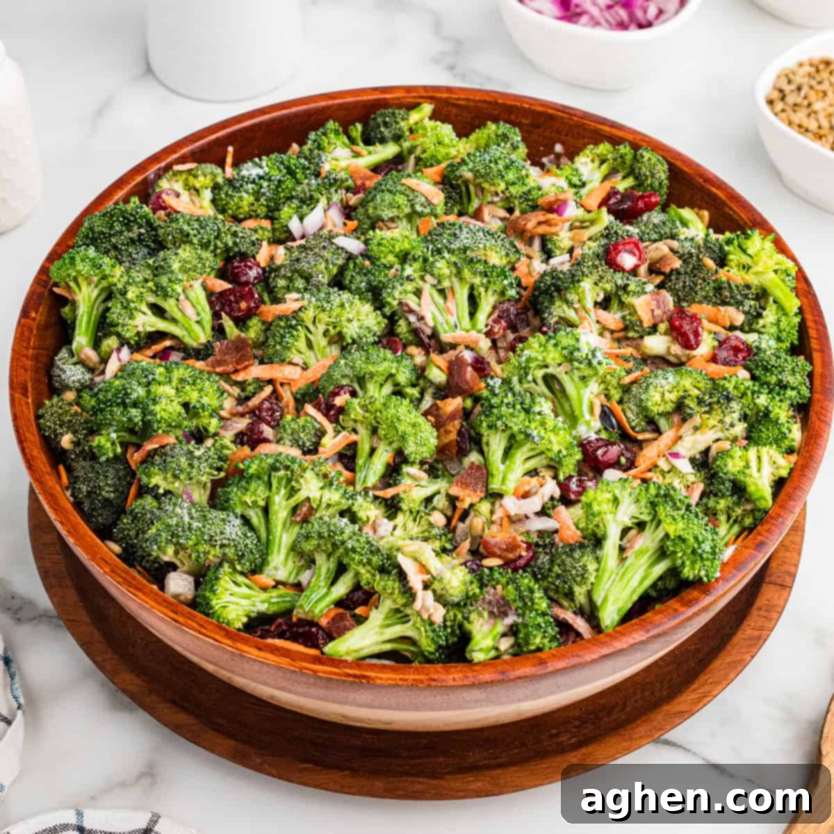 Super Crunchy Broccoli Delight 2 A large wooden bowl filled with broccoli crunch salad, made with fresh broccoli, bacon bits, dried cranberries, shredded carrots, sunflower seeds, and chopped red onions, all lightly coated in a creamy dressing.