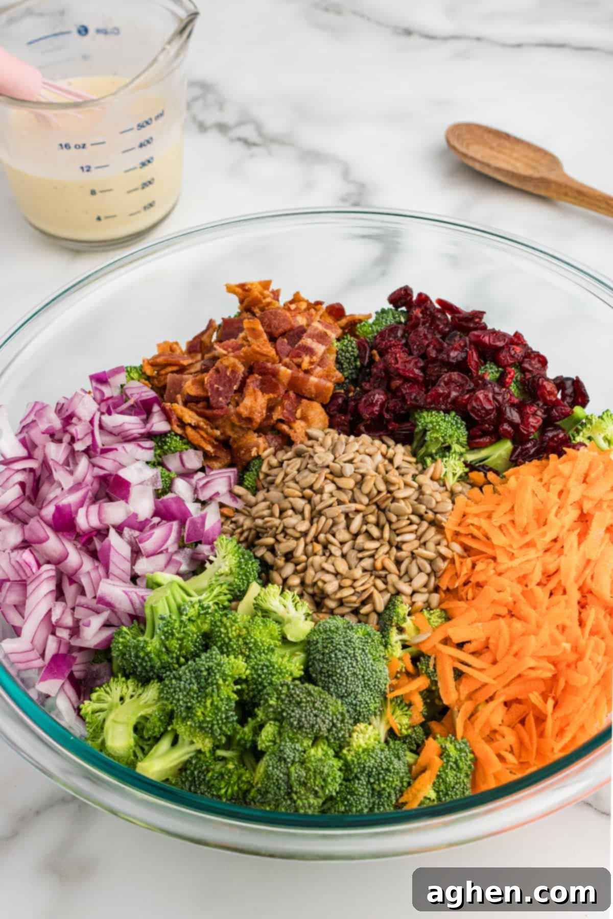 Super Crunchy Broccoli Delight 4 A glass bowl with ingredients for broccoli crunch salad, including broccoli, carrots, bacon, cranberries, onions, and sunflower seeds.