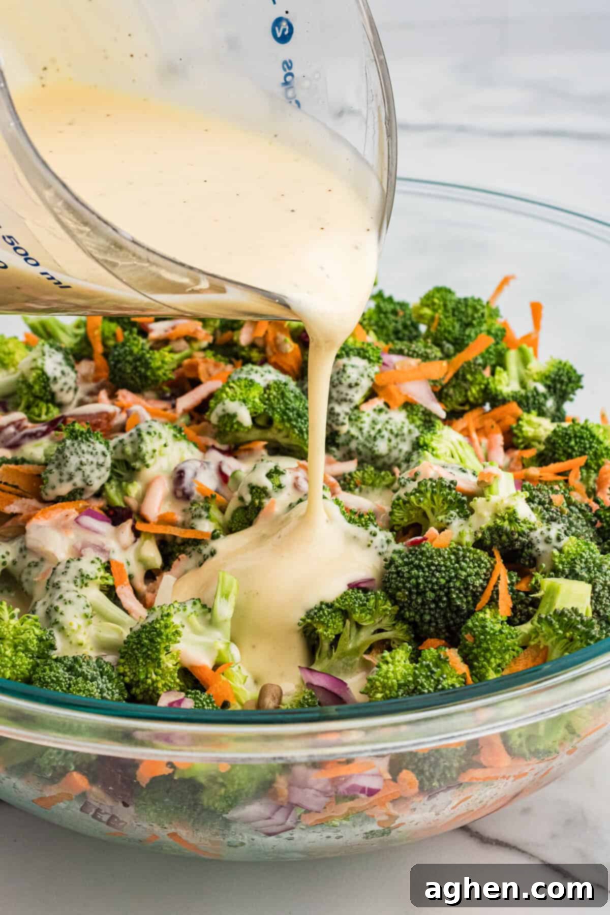 Super Crunchy Broccoli Delight 6 A close-up of creamy dressing being poured from a glass measuring cup over a bowl of broccoli crunch salad.