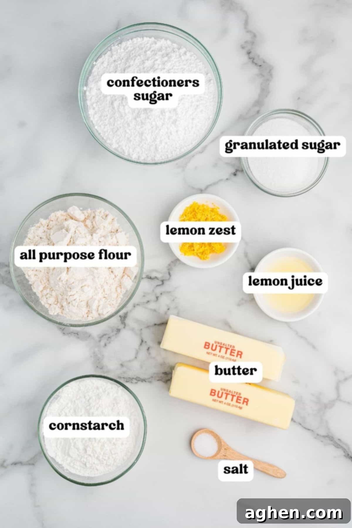Ingredients for lemon shortbread cookies on a marble surface, including flour, butter, cornstarch, confectioners sugar, granulated sugar, lemon zest, lemon juice, and salt. 