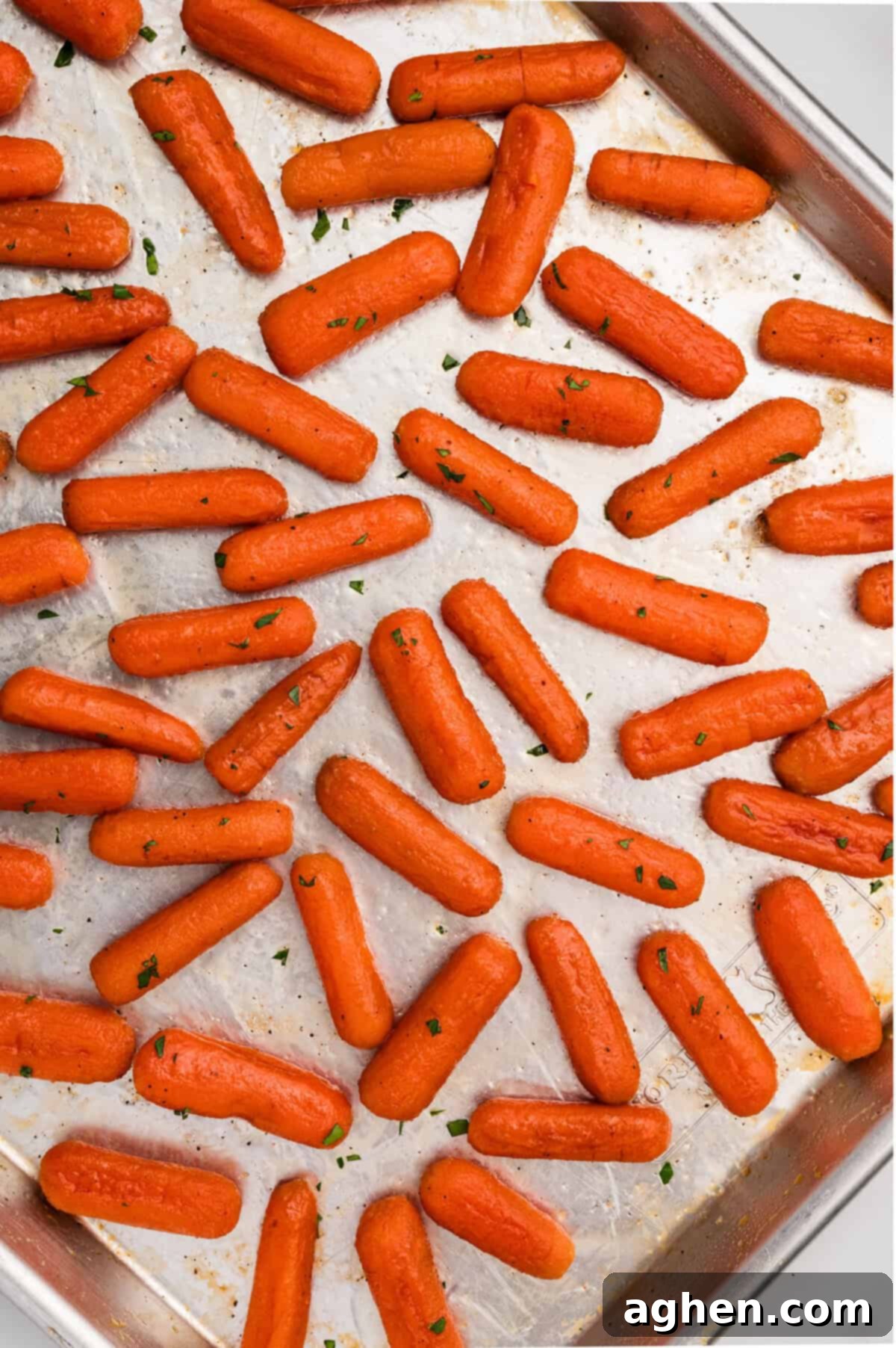 A sheet pan filled with a single layer or roasted baby carrots coated in a brown sugar honey glaze.