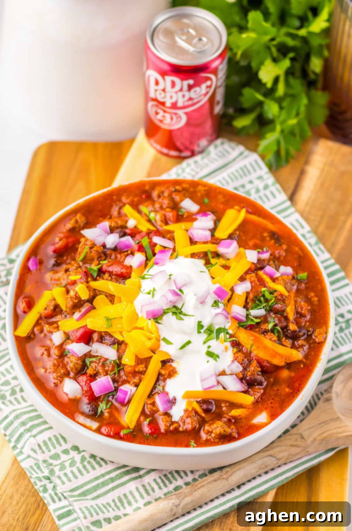 Bowl of crockpot Dr pepper chili with toppings next to a can of Dr Pepper.