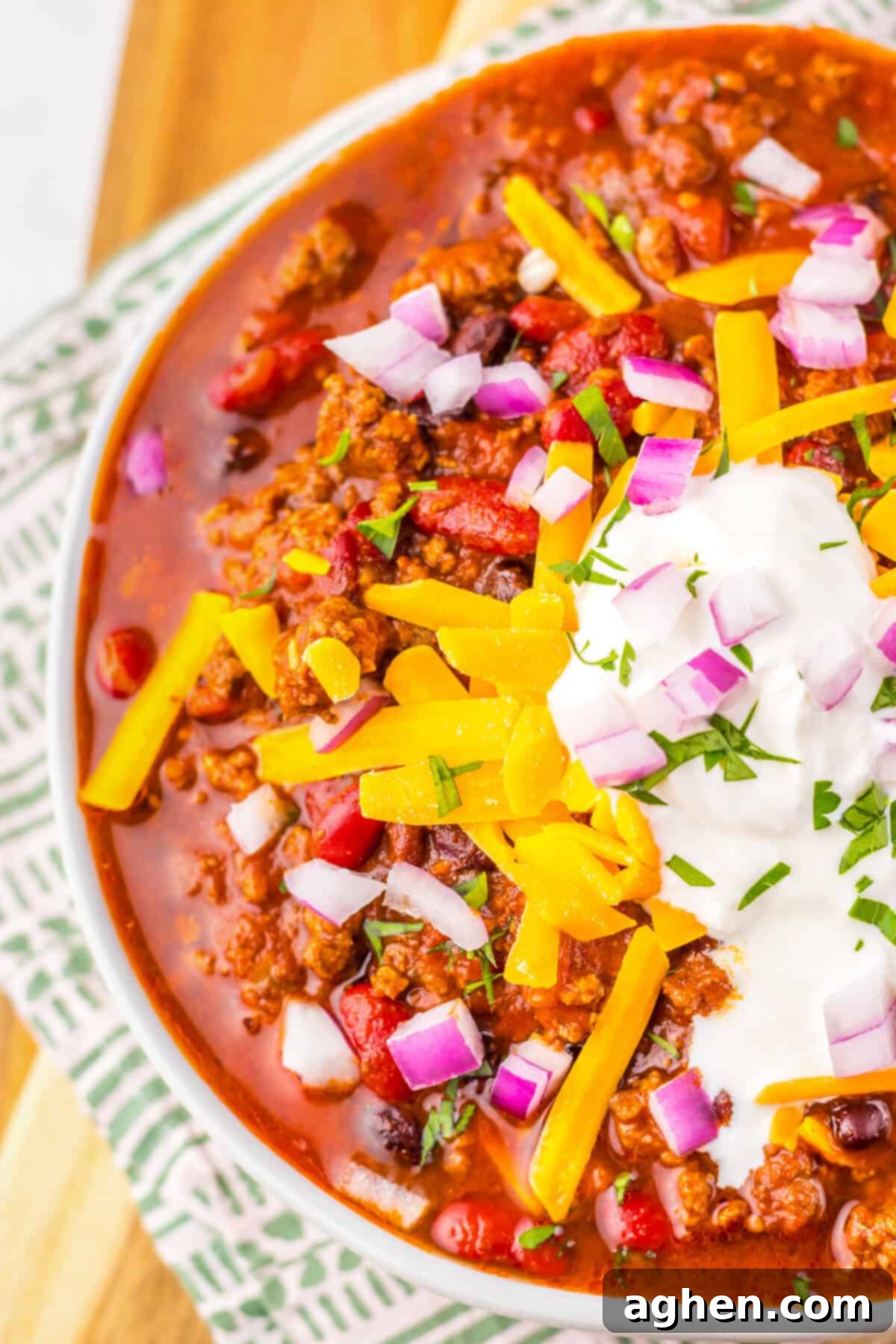 A bowl of Dr. Pepper Chili topped with cheese, sour cream, onions, and herbs.
